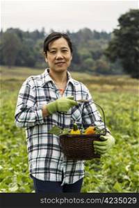 Mature women standing in bean field with basket of vegetables with trees and sky in background