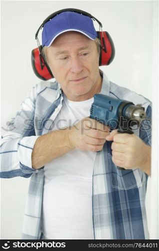mature worker with a drill and ear plugs