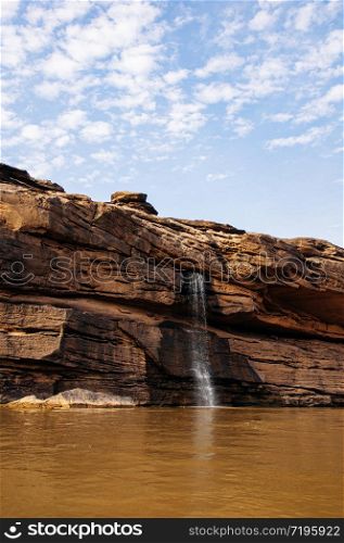 MAY 17, 2010 , Ubon Ratchathani, Thailand - Large Sand stone canyon cliff shoreline and waterfall pouring onto Mekong river with blue sky at Ban Pha Chan.