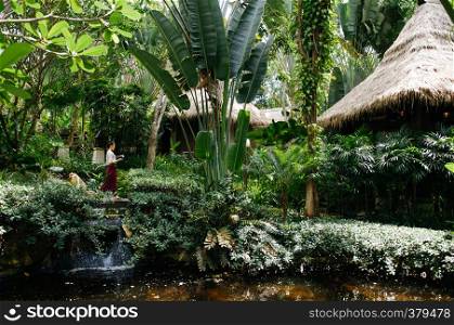 MAY 18, 2014 Krabi, THAILAND - Woman holding tray in lush green island tropical garden. Asian tropical garden landscaping design