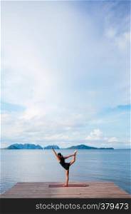 MAY 20, 2014 Koh lanta, Krabi, Thailand - Asian woman doing standing yoga pose on the wooden pier by the sea on clear blue sky day in summer.