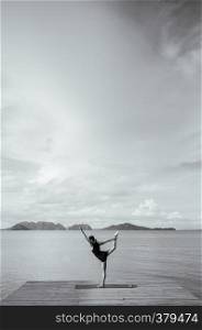 MAY 20, 2014 Koh lanta, Krabi, Thailand - Asian woman doing yoga pose on the wooden pier by the sea on clear sky day in summer. Black and white image.
