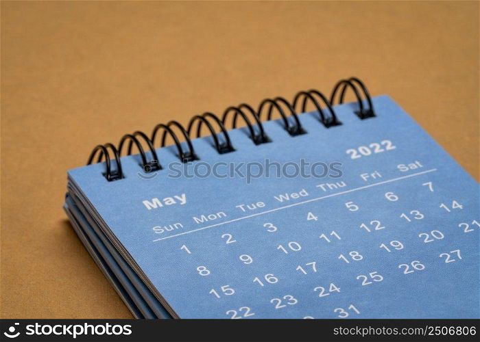 May 2022 - spiral desktop calendar against textured handmade paper, low angle macro shot, time and business concept
