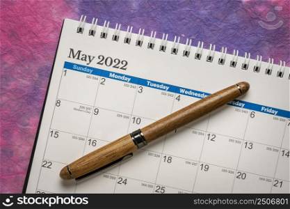 May 2022 - spiral desktop calendar with a stylish pen against colorful marbled paper,  time and business concept