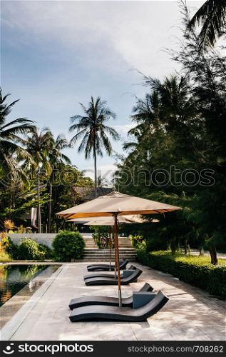 MAY 21, 2014 Krabi, THAILAND - Resort pool in tropical coconut garden, umbrellas and pool beds, Koh Lanta tropical resort outdoor space in summer
