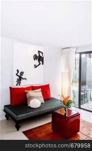MAY 22,2014 Koh Lanta, Krabi, Thailand - White modern minimal living room interior with colorful furnitures, picture frame, black sofa couch with asian style pillows and red acrylic table. Modern simple and clean interior design