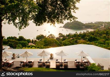 MAY 22, 2014 Krabi, THAILAND - Hill top pool under big tree with seascape, white umbrellas and sunbeds, Koh Lanta tropical resort outdoor space in summer
