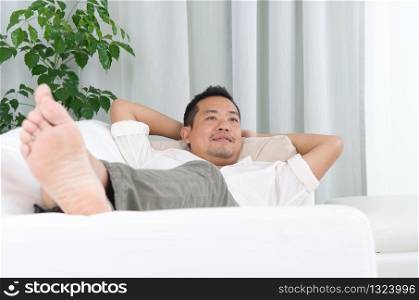 May guy resting and daydreaming at home. Asian handsome man relaxed and lying on sofa indoor.