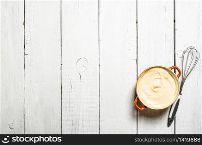 Mayonnaise in bowl with whisk. On a white wooden background.. Mayonnaise in bowl with whisk.