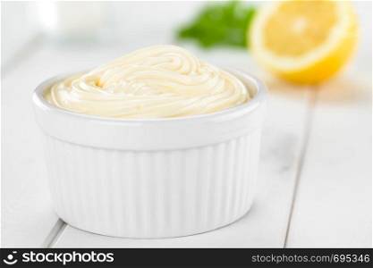 Mayonnaise sauce in white bowl with salt, lemon and parsley in the back (Selective Focus, Focus in the middle of the mayonnaise). Mayonnaise