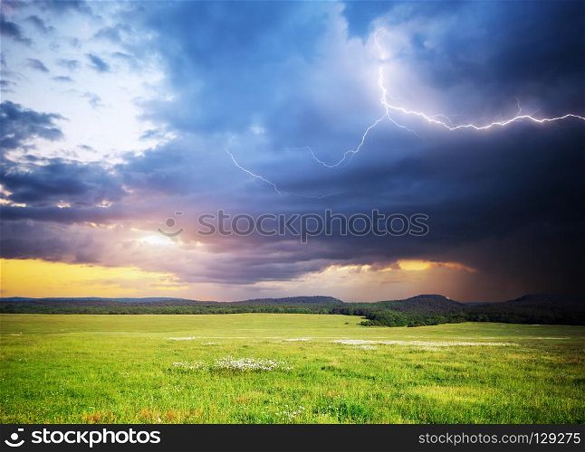 Meadow in mountain. Rain cloud and lightning. Nature composition.