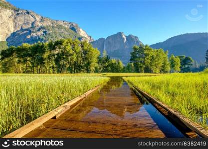 Meadow with flooded boardwalk in Yosemite National Park Valley with Yosemite Falls. California, USA.