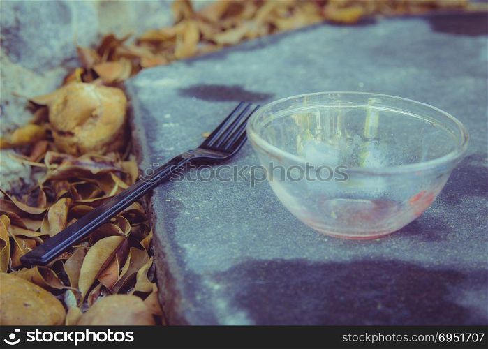 Meal in the garden - Close up on black plastic fork and a small empty glass bowl that are placed on a black stone in the garden. Many orange leaves all around. Selective Focus.