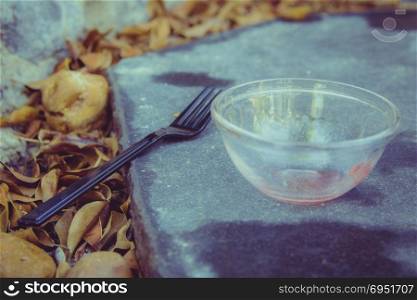 Meal in the garden - Close up on black plastic fork and a small empty glass bowl that are placed on a black stone in the garden. Many orange leaves all around. Selective Focus.