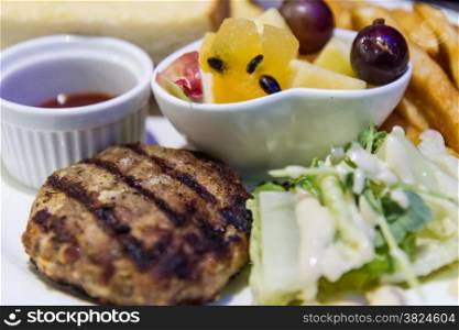 Meal with hamburger patty and vegetables and fruit salad