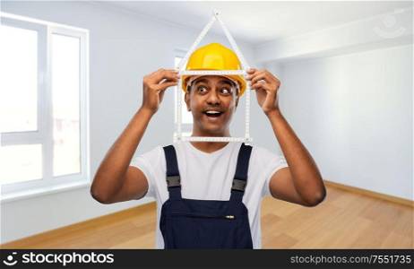 measurement, construction and building concept - happy smiling indian repairman or builder in helmet with folding ruler in shape of home over empty room background. happy indian builder with ruler in shape of home
