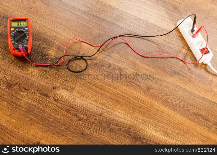 Measurement of voltage in electrical socket extension cord with multimeter on wooden floor background. Measurement voltage in electrical socket with multimeter