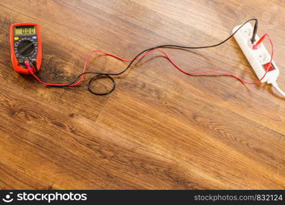 Measurement of voltage in electrical socket extension cord with multimeter on wooden floor background. Measurement voltage in electrical socket with multimeter