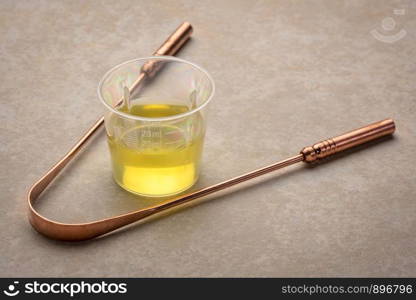 measuring cup of pulling oil and a copper tongue scrapper, oral hygiene concept