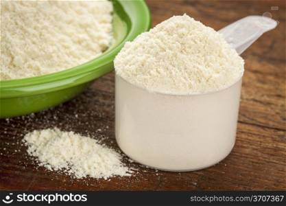 measuring scoop of whey protein powder with a bowl on wooden surface