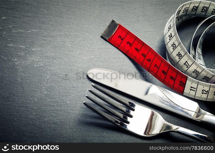 Measuring tape, knife and fork on grey background - diet concept