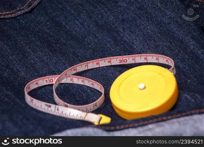 Measuring tape with a yellow color on the denim jeans material with a blue color