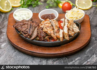 Meat and chicken fajitas on black stone plate with sauces