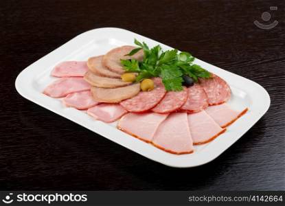 Meat assortment of beef tongue, sausage, meat and ham with greens