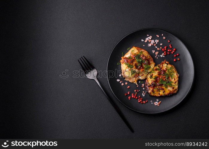 Meat baked in the oven with pineapple, tomatoes, cheese, spices and herbs on a black ceramic plate on a dark concrete background