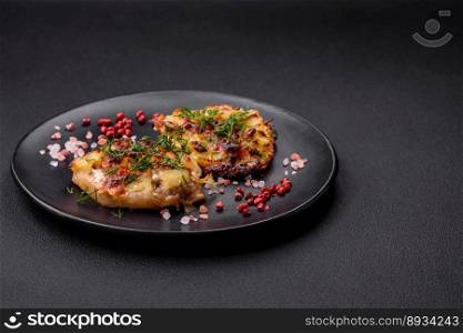 Meat baked in the oven with pineapple, tomatoes, cheese, spices and herbs on a black ceramic plate on a dark concrete background