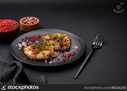 Meat baked in the oven with pineapple, tomatoes, cheese, spices and herbs on a black ceramic plate on a dark concrete background