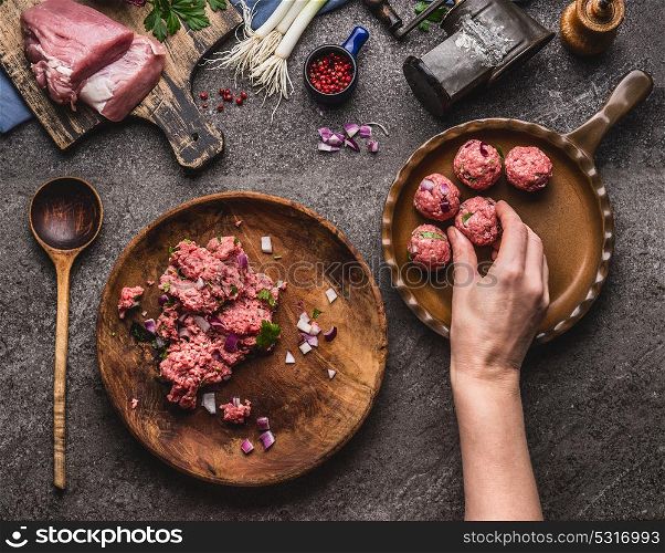 Meat balls making. Female hand puts meat ball in frying pan. Preparation on kitchen table with meat, force meat , meat grinder and spoon, top view. Cooking,recipes and eating concept