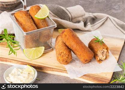Meat croquets with garlic mayonnaise, lime slices to season and rosemary leaves on wooden table in a kitchen counter top.