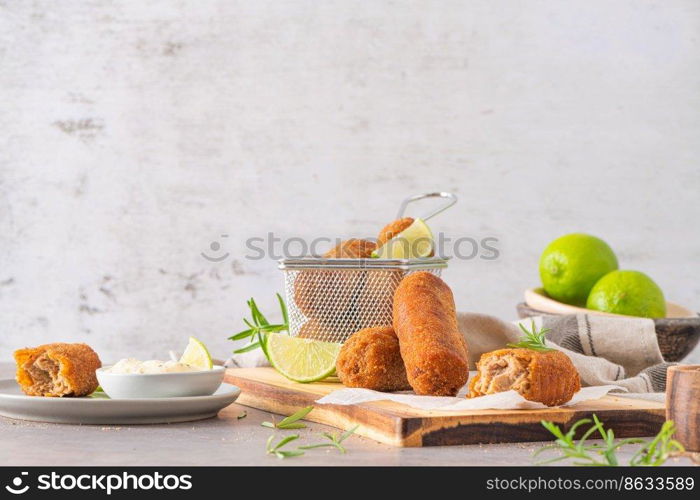 Meat croquets with garlic mayonnaise, lime slices to season and rosemary leaves on wooden table in a kitchen counter top.