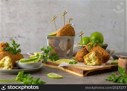 Meat croquets with rosemary leaves and lemons on wooden cutting board in a kitchen counter top.