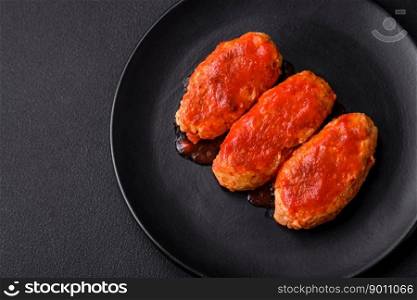 Meat cutlet or meatballs in tomato sauce with garlic, salt, spices and herbs on a black plate on a dark concrete background