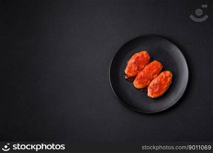 Meat cutlet or meatballs in tomato sauce with garlic, salt, spices and herbs on a black plate on a dark concrete background