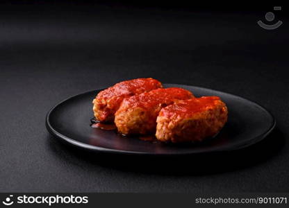 Meat cutlet or meatballs in tomato sauce with garlic, salt, spices and herbs on a black plate on a dark concrete background