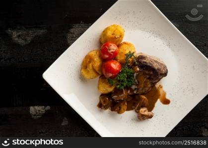 meat dish on a wooden old surface. fried meat with potatoes in a white plate on a wooden old board. dish on a wooden surface