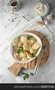 Meat dumplings - russian pelmeni, ravioli with meat on a white plate on a wooden serving board. Flat lay composition