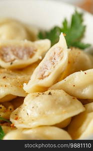 Meat dumplings - russian pelmeni, ravioli with meat on a white plate on a wooden serving board