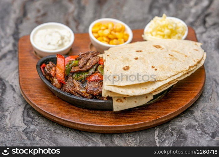 Meat fajitas on black stone plate with sauces