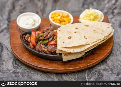 Meat fajitas on black stone plate with sauces