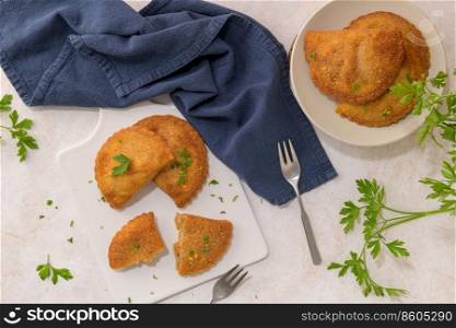 Meat patties and parsley leaves on white ceramic dishes in a kitchen counter top.