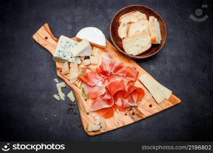 Meat plate of Italian prosciutto crudo or spanish jamon and cheede on wooden cutting board. Concrete background. Meat plate of Italian prosciutto crudo or spanish jamon and cheese