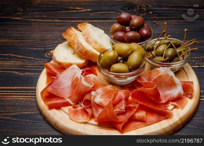 Meat plate of Italian prosciutto crudo or spanish jamon on wooden cutting board. Wooden background. Meat plate of Italian prosciutto crudo or spanish jamon on wooden cutting board