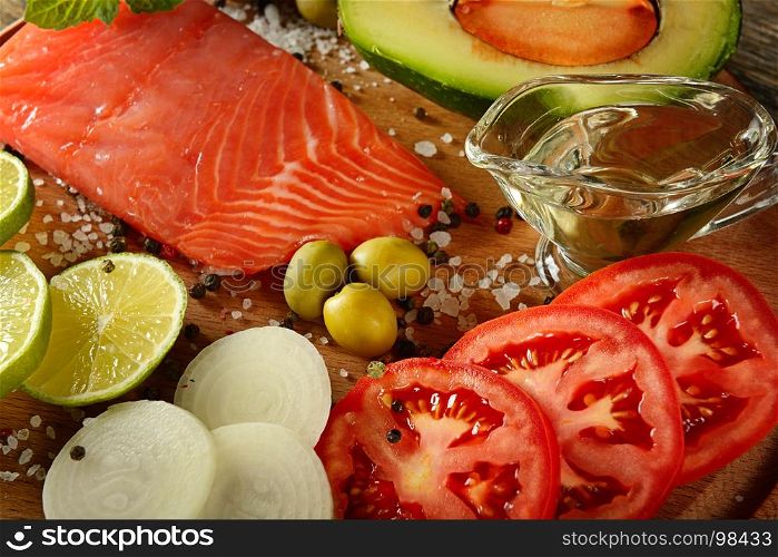 Meat red salmon fish, tomatoes, spices, green olives and olive oil on kitchen table. Top view. Selective focus.