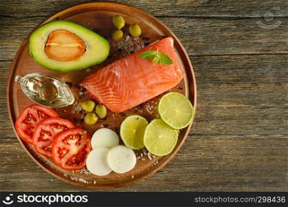 Meat red salmon fish, tomatoes, spices, lemon, green olives on wooden kitchen table. Copy space.