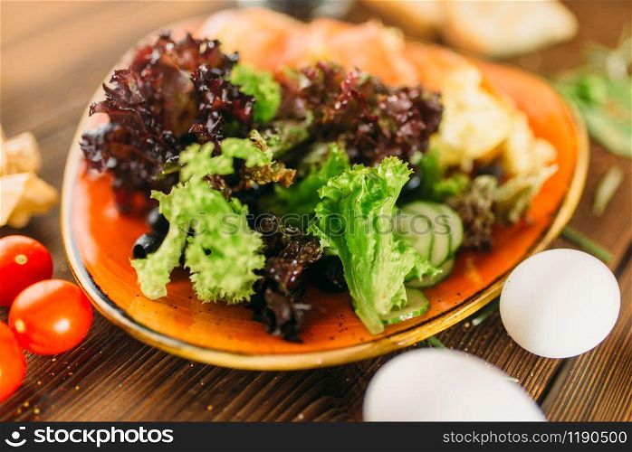 Meat salad in a bowl, knife, fork and pepperbox on wooden table, top view, nobody. Food preparation, cooking. Meat salad in a bowl on wooden table, top view