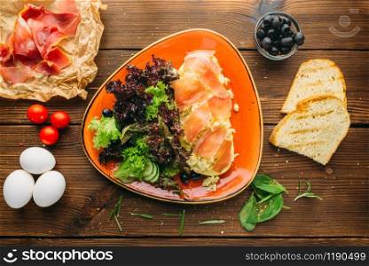 Meat salad in a bowl, olives, herb, bread and eggs on wooden table, top view, nobody. Food preparation, cooking
